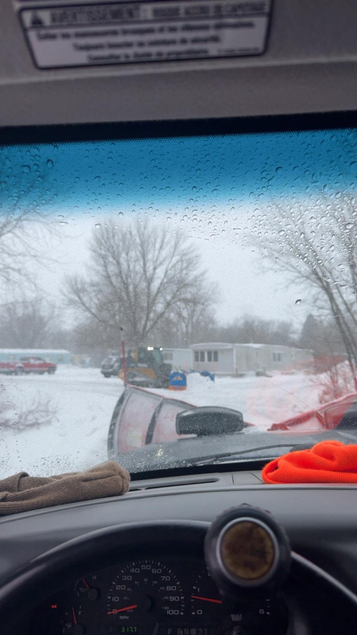 View from inside a truck during a snowstorm, with a loader moving snow outside
